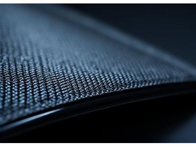 A gleaming, woven carbon fiber trim piece for a car interior, reflecting light.